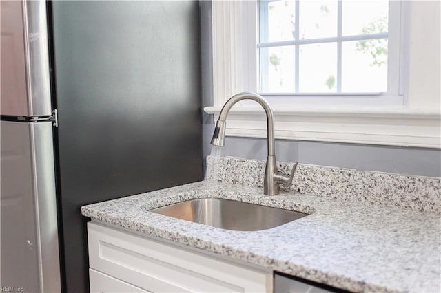 room details featuring white cabinets, stainless steel fridge, light stone counters, and sink