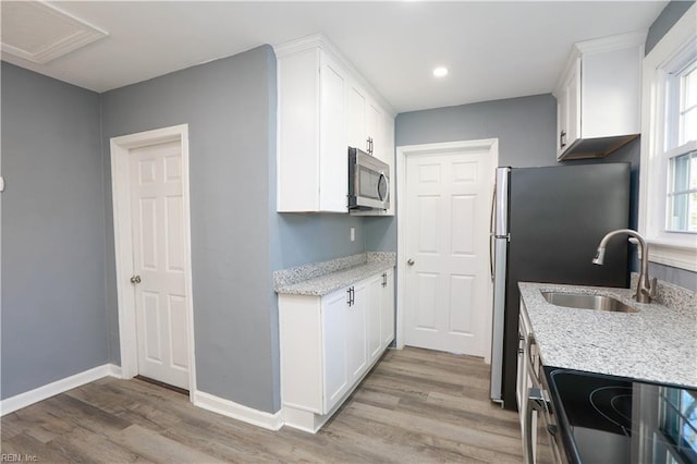 kitchen with white cabinets, appliances with stainless steel finishes, light hardwood / wood-style floors, and light stone counters