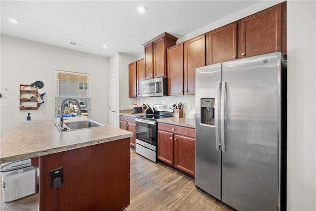 kitchen featuring sink, a kitchen breakfast bar, light hardwood / wood-style floors, a kitchen island with sink, and appliances with stainless steel finishes