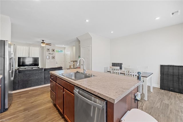 kitchen featuring a kitchen island with sink, sink, light hardwood / wood-style flooring, ceiling fan, and stainless steel appliances