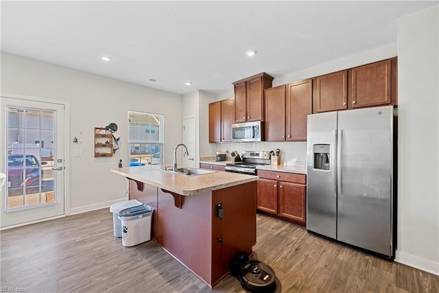 kitchen featuring a center island with sink, a kitchen breakfast bar, sink, light hardwood / wood-style flooring, and stainless steel appliances