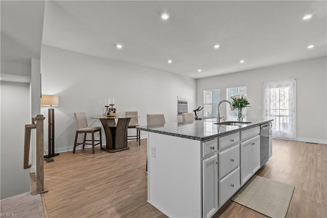 kitchen featuring dishwasher, sink, a kitchen breakfast bar, an island with sink, and dark stone counters