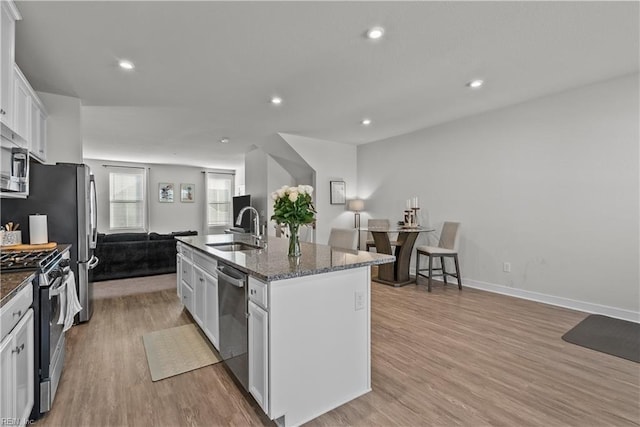 kitchen with white cabinets, a center island with sink, sink, light hardwood / wood-style floors, and stainless steel appliances