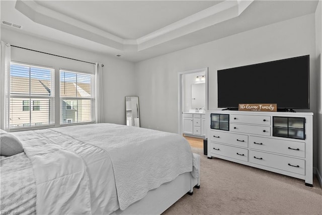 carpeted bedroom with ensuite bathroom and a tray ceiling