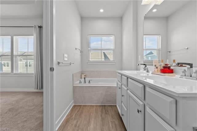 bathroom with hardwood / wood-style flooring, vanity, and tiled bath