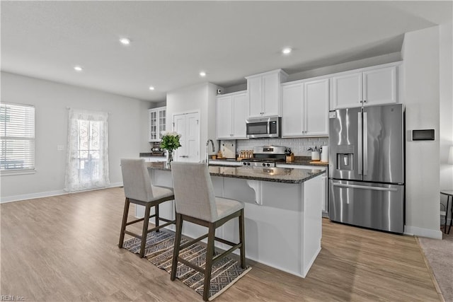 kitchen with white cabinetry, stainless steel appliances, dark stone countertops, a breakfast bar area, and a kitchen island with sink