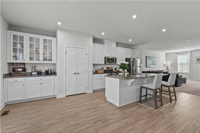 kitchen with dark stone counters, a kitchen island with sink, white cabinets, and stainless steel appliances