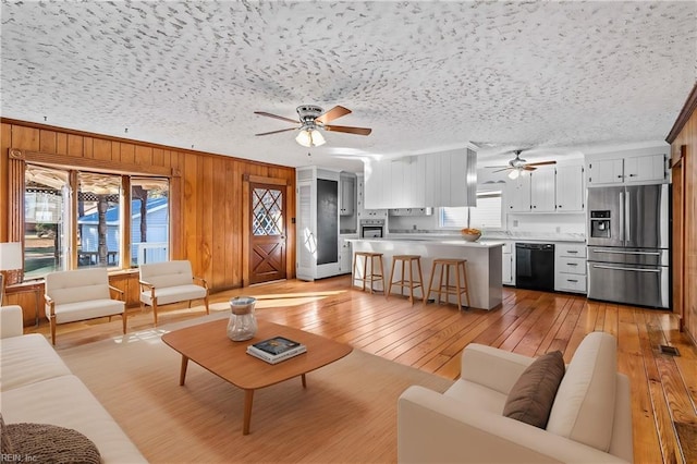 living room with wood walls, light hardwood / wood-style flooring, ceiling fan, and a textured ceiling