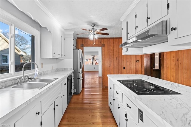 kitchen with wood walls, white cabinetry, black appliances, and sink