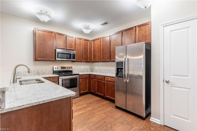 kitchen with kitchen peninsula, appliances with stainless steel finishes, light stone counters, sink, and light hardwood / wood-style flooring