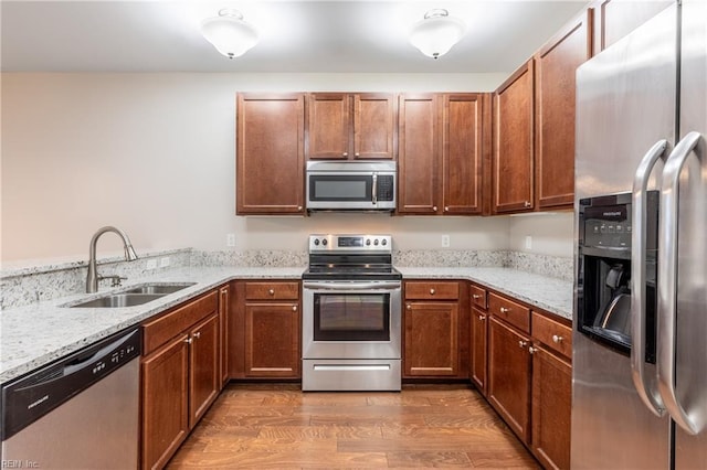 kitchen featuring light stone countertops, sink, kitchen peninsula, appliances with stainless steel finishes, and hardwood / wood-style flooring