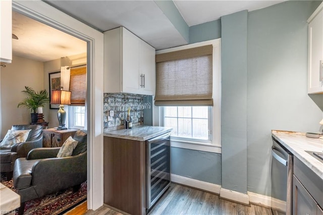 kitchen with decorative backsplash, light wood-type flooring, stainless steel dishwasher, white cabinets, and wine cooler