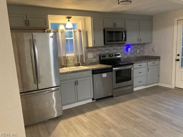 kitchen with appliances with stainless steel finishes, gray cabinets, light hardwood / wood-style flooring, and sink