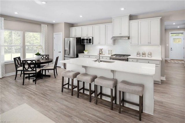 kitchen with a kitchen island with sink, white cabinets, sink, light wood-type flooring, and stainless steel appliances