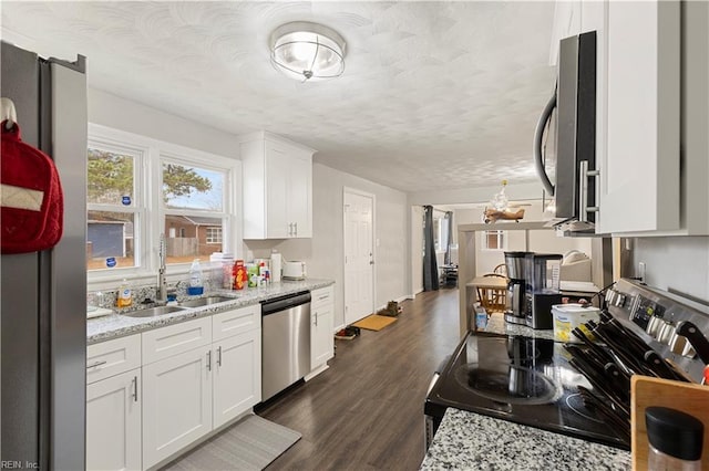 kitchen with appliances with stainless steel finishes, dark hardwood / wood-style flooring, light stone counters, sink, and white cabinets