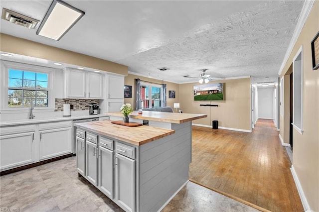 kitchen featuring white cabinetry, ceiling fan, butcher block countertops, decorative backsplash, and a kitchen island