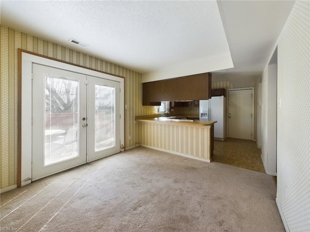 kitchen featuring french doors, white fridge with ice dispenser, a textured ceiling, light colored carpet, and kitchen peninsula