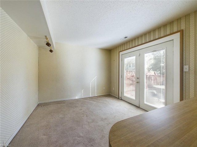 empty room featuring french doors, a textured ceiling, and light colored carpet