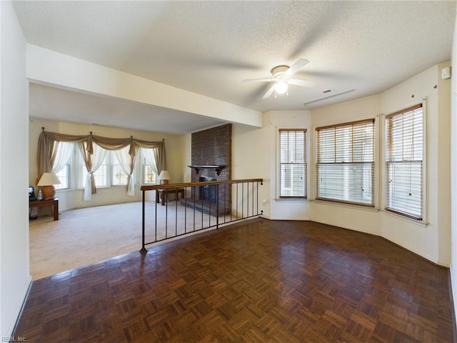 spare room featuring a fireplace, a textured ceiling, ceiling fan, and dark parquet floors