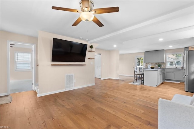 unfurnished living room featuring beam ceiling, ceiling fan, sink, and light hardwood / wood-style floors