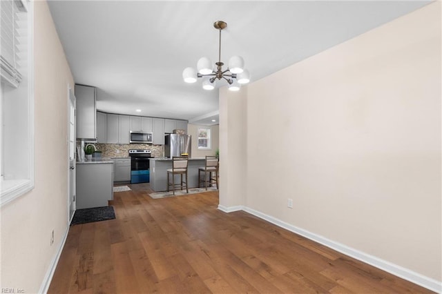 kitchen featuring backsplash, stainless steel appliances, decorative light fixtures, an inviting chandelier, and hardwood / wood-style flooring