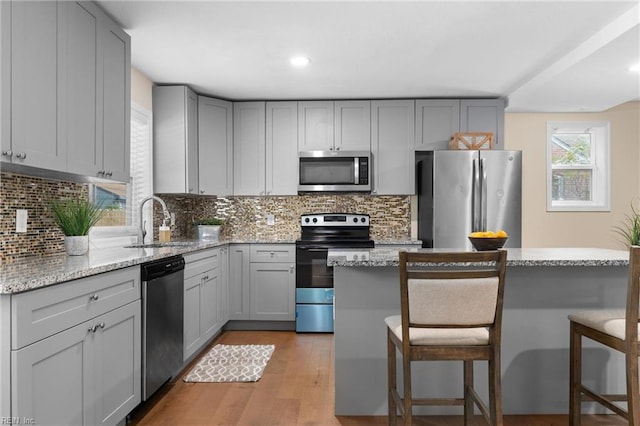 kitchen featuring light stone countertops, sink, stainless steel appliances, gray cabinets, and a kitchen island