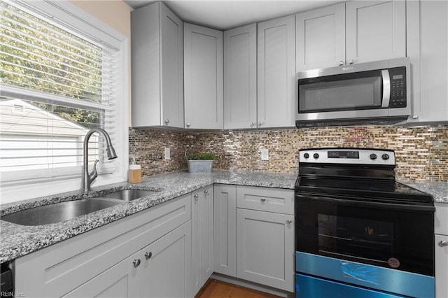 kitchen with decorative backsplash, stainless steel appliances, light stone countertops, and sink