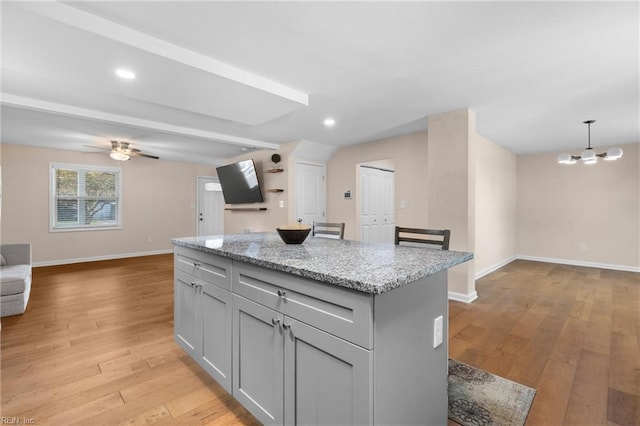 kitchen with light stone countertops, pendant lighting, gray cabinets, a kitchen island, and ceiling fan with notable chandelier