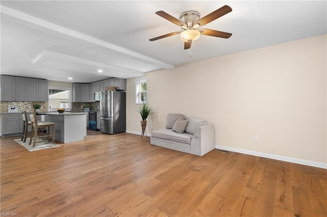 unfurnished living room featuring beam ceiling, ceiling fan, light hardwood / wood-style flooring, and a healthy amount of sunlight