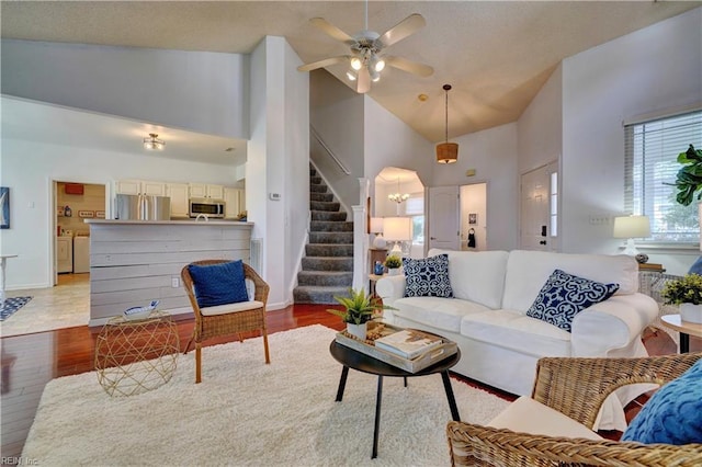 living room featuring ceiling fan with notable chandelier, washing machine and dryer, light wood-type flooring, and high vaulted ceiling