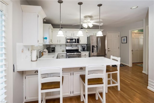 kitchen with hanging light fixtures, kitchen peninsula, appliances with stainless steel finishes, a kitchen bar, and white cabinetry