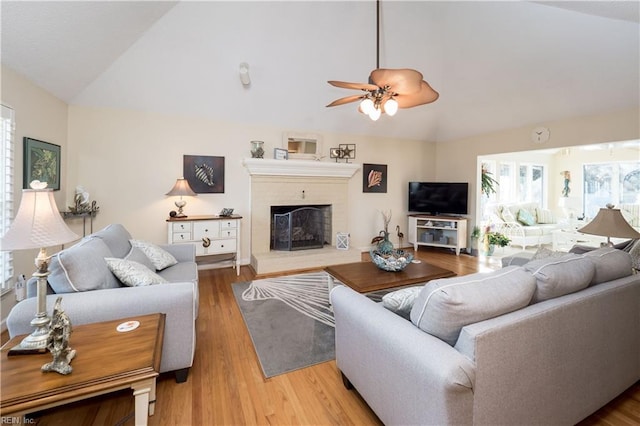 living room with ceiling fan, vaulted ceiling, a fireplace, and light hardwood / wood-style flooring