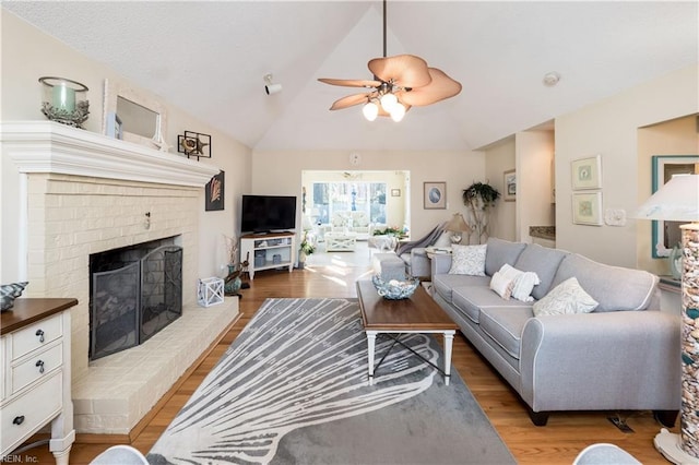 living room featuring ceiling fan, light hardwood / wood-style flooring, vaulted ceiling, and a brick fireplace