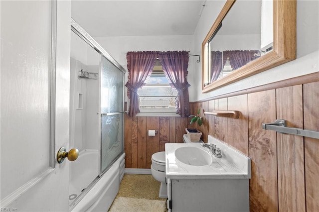 full bathroom with combined bath / shower with glass door, vanity, toilet, and wooden walls