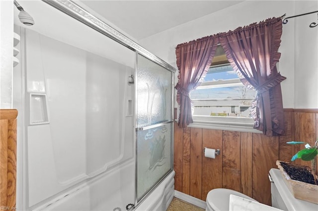 bathroom with toilet, enclosed tub / shower combo, and wooden walls