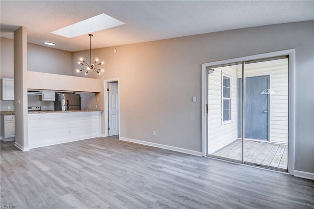 unfurnished living room with vaulted ceiling with skylight, an inviting chandelier, a textured ceiling, and hardwood / wood-style flooring