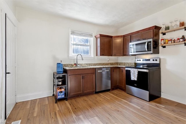 kitchen with appliances with stainless steel finishes, light stone counters, light hardwood / wood-style flooring, and sink