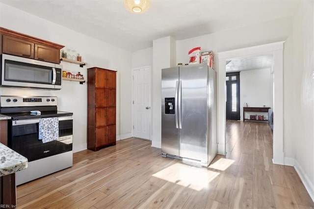 kitchen with appliances with stainless steel finishes, light hardwood / wood-style flooring, and light stone counters