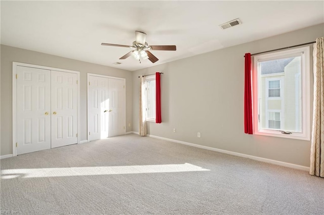 unfurnished bedroom with light colored carpet, ceiling fan, and multiple closets