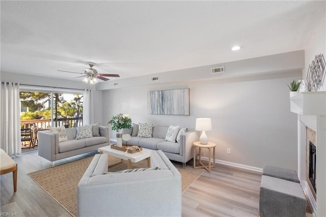 living room featuring ceiling fan, a fireplace, and light hardwood / wood-style flooring