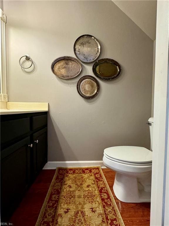 bathroom featuring vanity, wood-type flooring, vaulted ceiling, and toilet