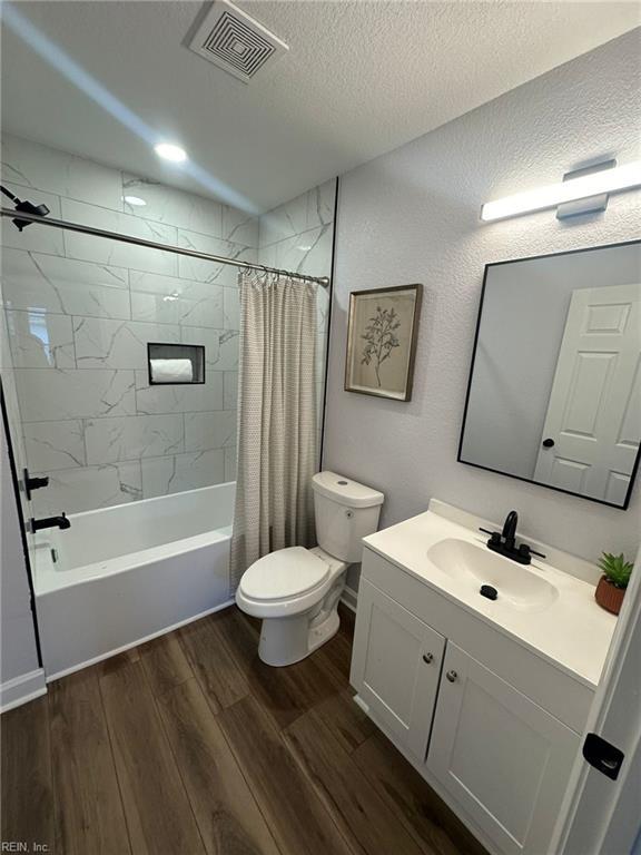 full bathroom with vanity, hardwood / wood-style flooring, toilet, a textured ceiling, and shower / tub combo with curtain