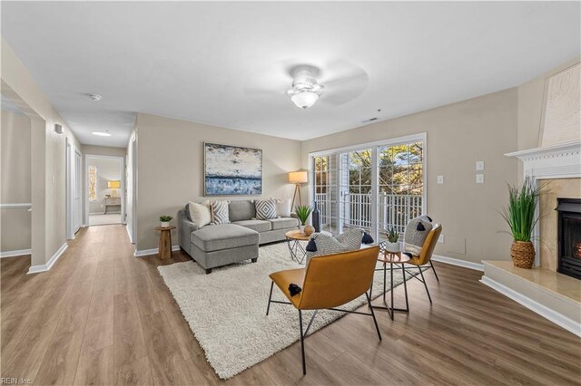 living room with a tile fireplace, ceiling fan, and light wood-type flooring