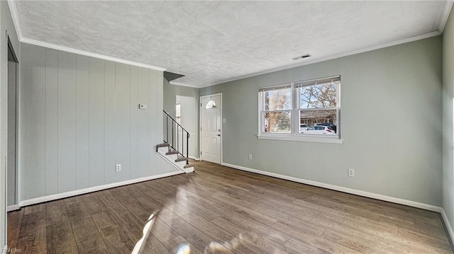 unfurnished room featuring hardwood / wood-style floors, a textured ceiling, ornamental molding, and wood walls