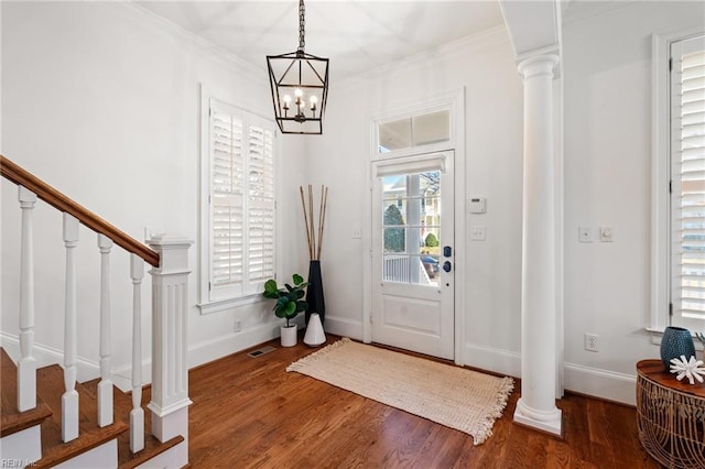 entryway with an inviting chandelier, crown molding, dark wood-type flooring, and ornate columns