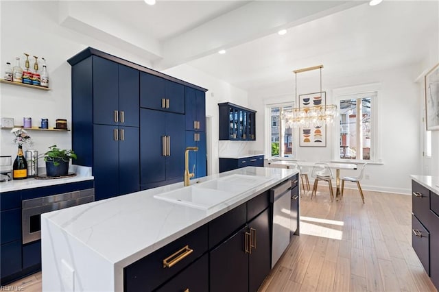 kitchen featuring blue cabinetry, sink, stainless steel appliances, light hardwood / wood-style floors, and a center island with sink