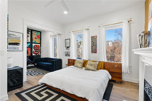 bedroom featuring ceiling fan, light hardwood / wood-style floors, and a fireplace