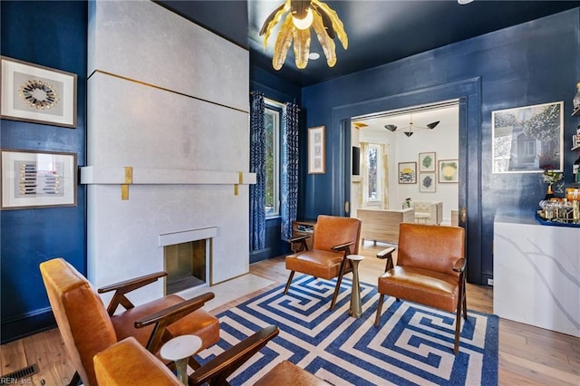 living area featuring a large fireplace, light wood-type flooring, and a chandelier