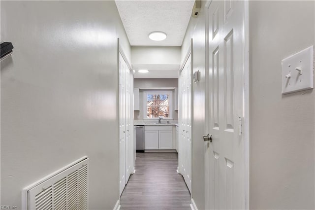 corridor with a textured ceiling, sink, and hardwood / wood-style floors