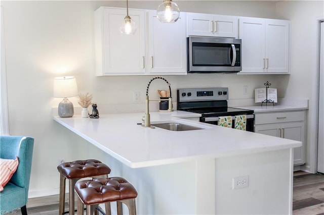 kitchen featuring a kitchen breakfast bar, kitchen peninsula, decorative light fixtures, white cabinetry, and stainless steel appliances